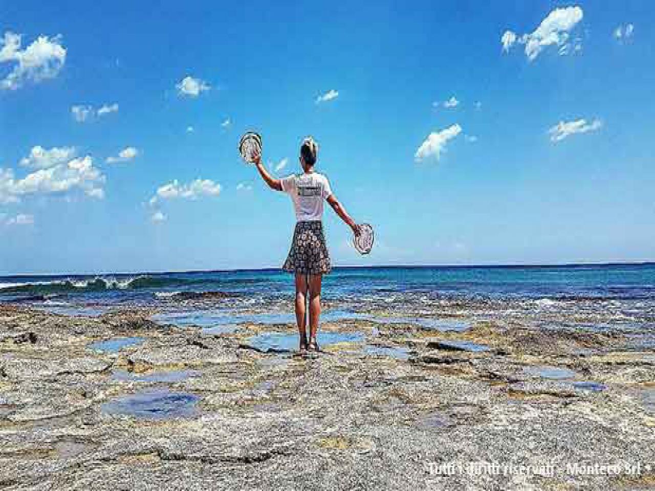 donna che cammina sulla spiaggia con in mano ruota dei rifiuti